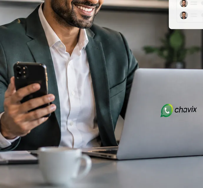 Corretor sorrindo com o celular na mão diante do notebook com o adesivo do Chavix, acompanhando os clientes do dia.